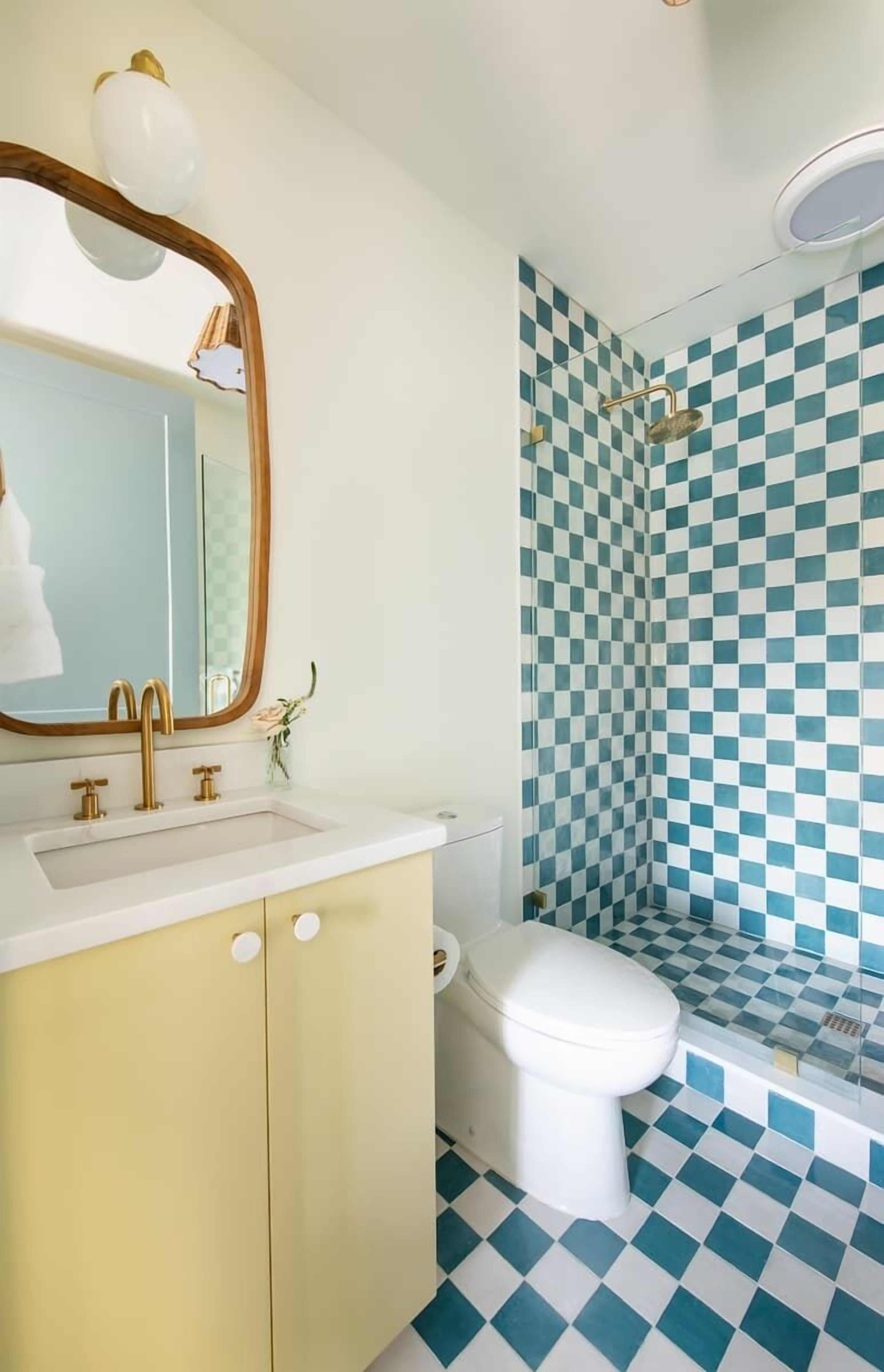 A bathroom with a checkered floor, a white sink with gold faucets, and a white toilet.