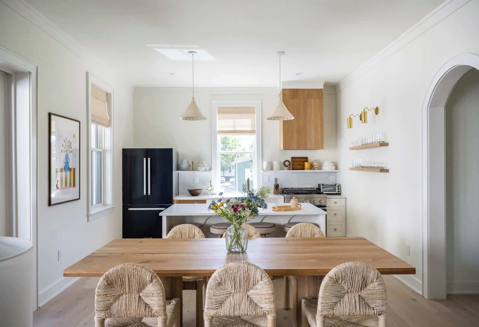 A modern kitchen with a wooden dining table, black refrigerator, and white cabinetry.