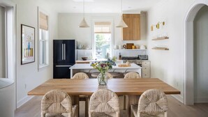 A modern kitchen with a wooden dining table, black refrigerator, and white cabinetry.
