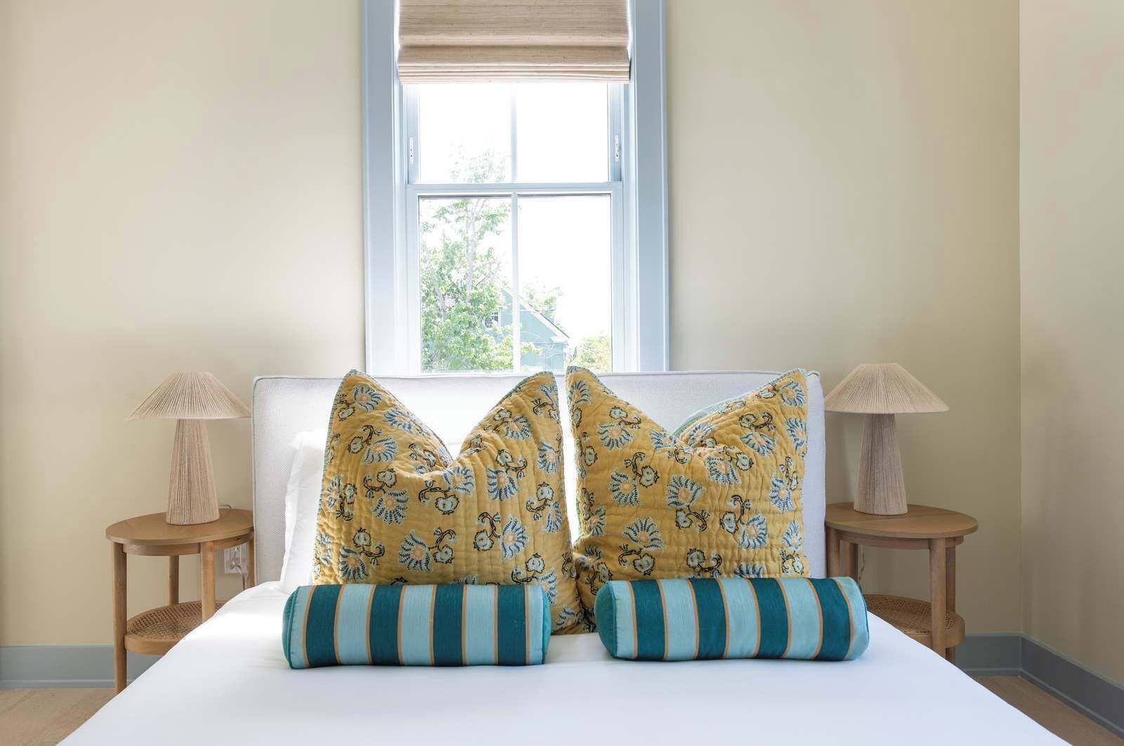 A bed with two decorative pillows, a window with a view, and two bedside lamps on wooden nightstands.