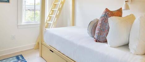 A bunk bed with a ladder, white bedding, and a patterned rug.