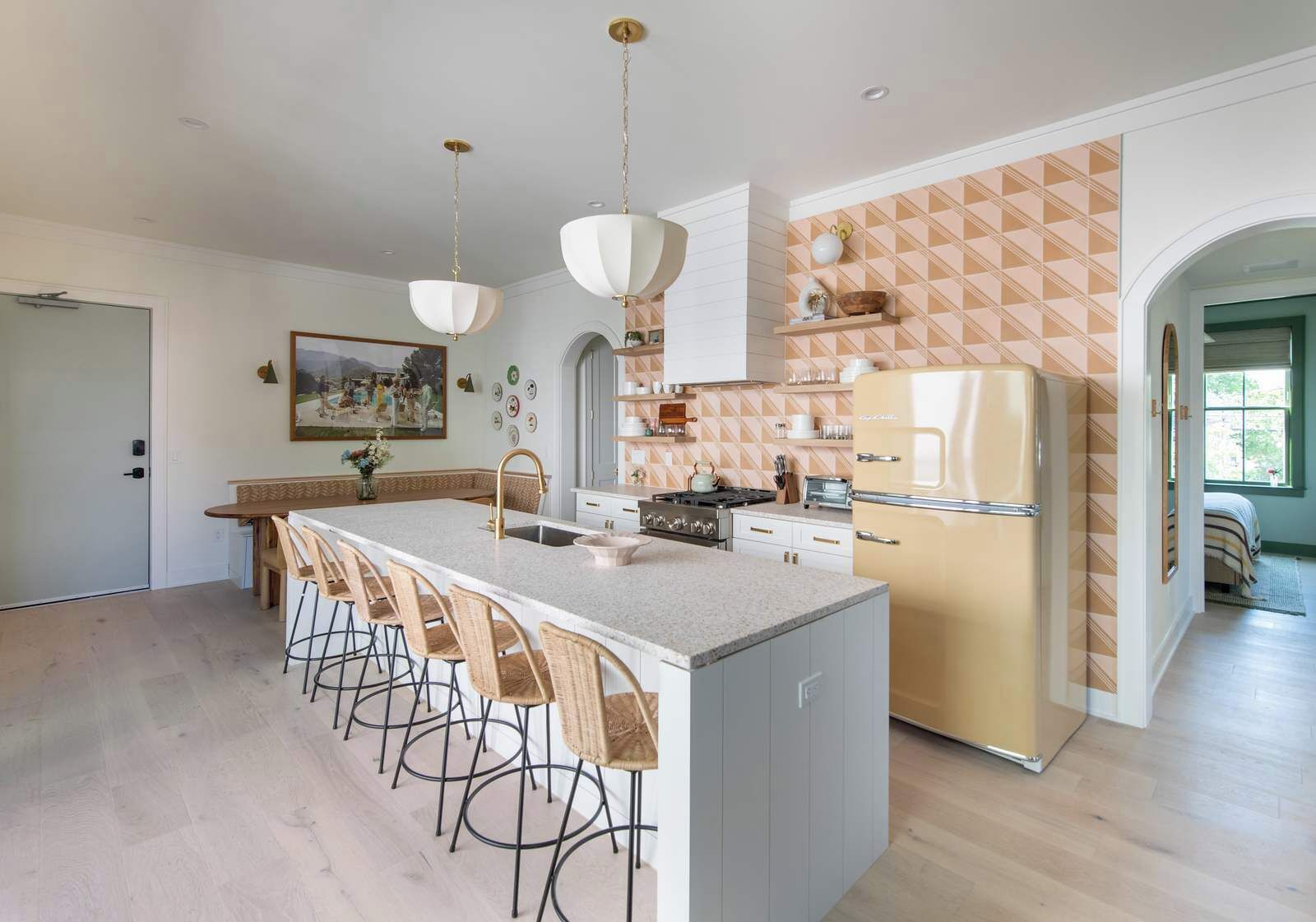 A modern kitchen with a central island, bar stools, a refrigerator, and a dining area with a painting on the wall.