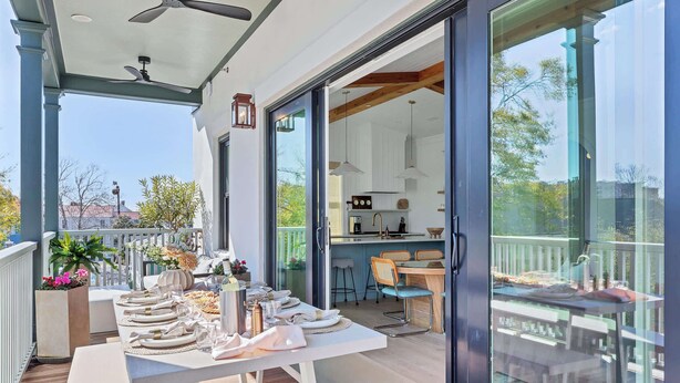 Un área de comedor al aire libre con una mesa preparada para seis personas, un ventilador de techo y vistas al jardín trasero a través de puertas de vidrio.