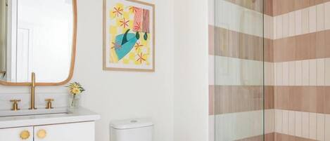 Un baño con lavamanos blanco, inodoro y cabina de ducha con mampara de vidrio.