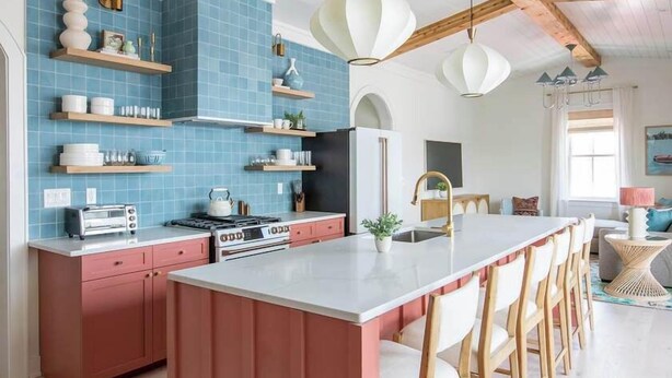 Une cuisine dotée d’un îlot central, de poutres en bois, de carreaux bleus et de luminaires suspendus.