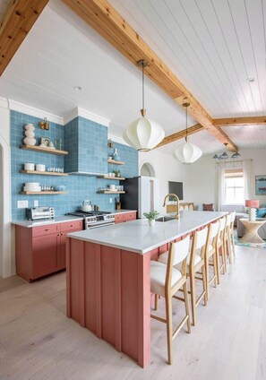 A kitchen with a central island, wooden beams, blue tiles, and pendant lighting.