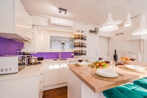 A modern kitchen with white cabinetry, a purple accent wall, and a dining area with a teal bench. - Charming Downtown Studio (Zagreb)