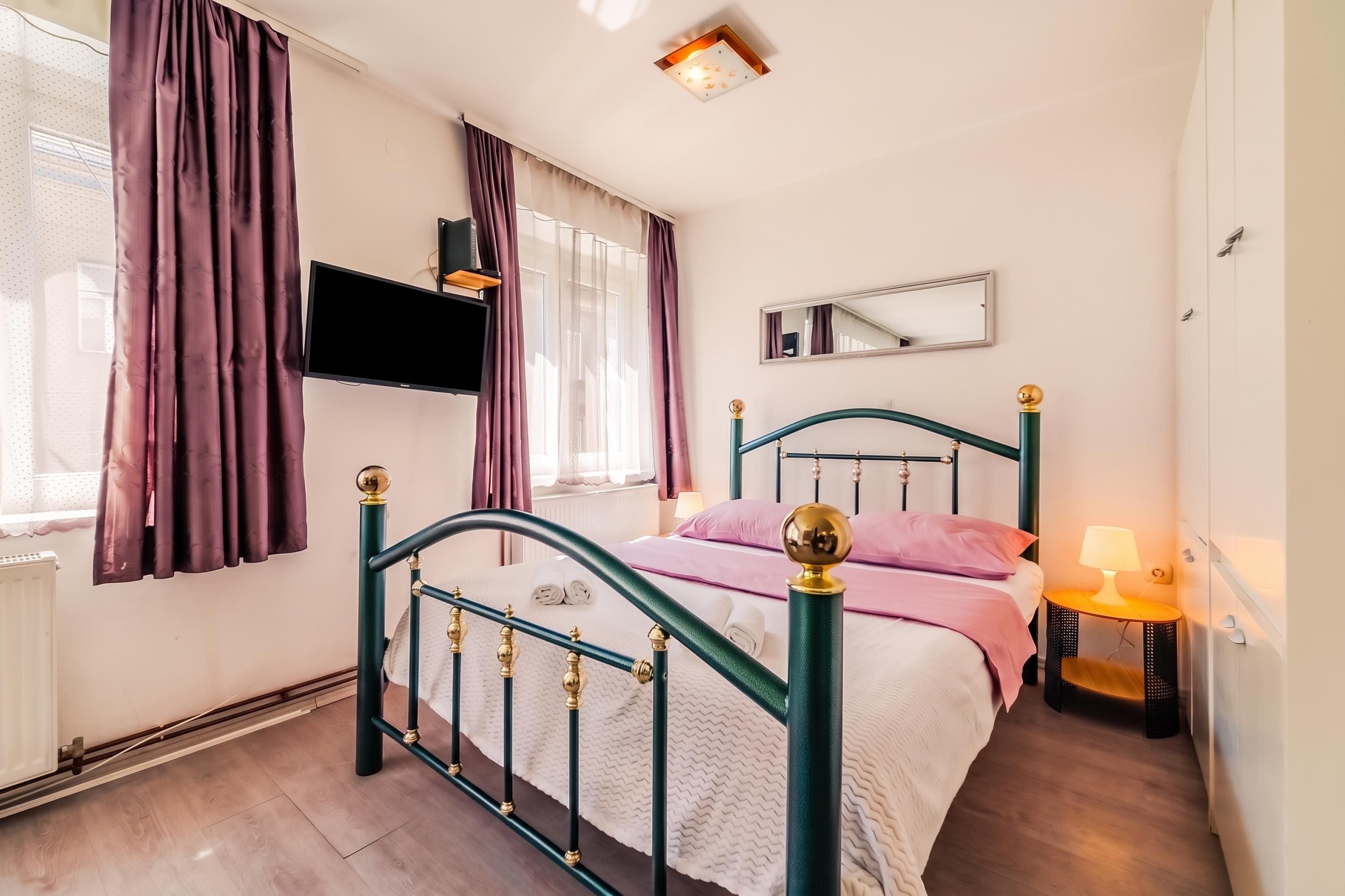 A bedroom with a bed, a bedside table, a lamp, a TV, and a window with curtains.