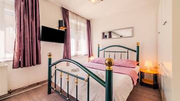 A bedroom with a bed, a bedside table, a lamp, a TV, and a window with curtains.