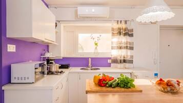 A modern kitchen with white cabinets, a purple wall, a window with a view, and a wooden countertop with vegetables.