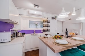 A modern kitchen with white cabinets, a purple backsplash, and a dining area with a wooden table set for two.