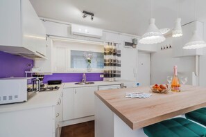A modern kitchen with white cabinets, a purple backsplash, and a wooden island with seating. - Charming Downtown Studio (Zagreb)