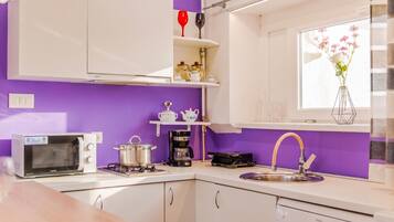 A compact kitchen with white cabinets, a microwave, a coffee maker, and a sink.