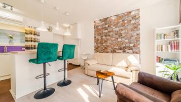 A modern living room with a sofa, two green chairs, a coffee table, and a bookshelf.