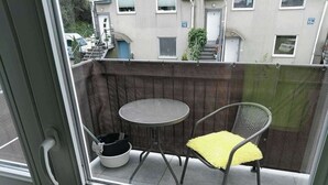 Un balcón con una mesa redonda, una silla, un cubo blanco y una valla metálica.