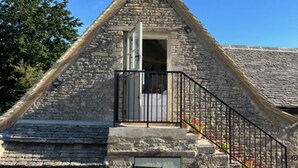 A stone building with a gabled roof, a small balcony with a black railing, and a garage door. - Idyllic secluded hideaway with countryside views (Hailey)