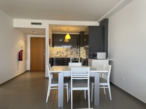 Une cuisine moderne avec un coin repas, comprenant une table et des chaises blanches, un four encastré et un four à micro-ondes.