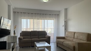 Ein Wohnzimmer mit einem beigen Sofa, einem weißen Couchtisch und einem Fernseher auf einem Lowboard.