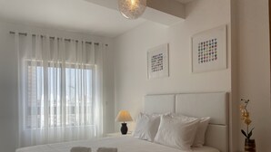 Ein Hotelzimmer mit einem großen Bett, weißen Vorhängen, einer Nachttischlampe und zwei gerahmten Kunstwerken an der Wand.