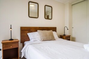 A neatly made bed with white linens, two bedside tables with lamps, and two wall mirrors.