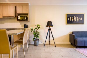 A compact living space with a kitchenette, a dining area, a seating area with a sofa, and a floor lamp.