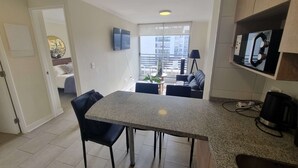 Eine moderne Küche mit Granitplatte, schwarzen Stühlen, einem Esstisch, einem an der Wand befestigten Fernseher und Blick auf die Stadt durch große Fenster.