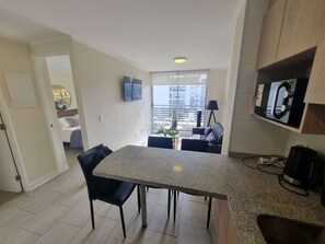 A modern kitchen with a granite countertop, black chairs, a dining table, a TV mounted on the wall, and a view of the city through large windows. - Modern 1BR Oasis in Centro | Steps to Toesca Metro (Unknown)