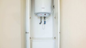 A white utility room with a water heater, a control panel, and a lower compartment. - Central Chic 1BR Steps from Metro & Attractions (Santiago)