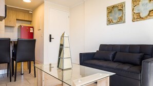 A modern living room with a glass coffee table, a black leather sofa, and a dining area with a red refrigerator. - Central Chic 1BR Steps from Metro & Attractions (Santiago)