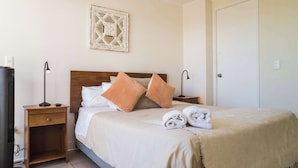 A neatly arranged hotel room with a bed, a nightstand, a lamp, a framed artwork, and a door. - Central Chic 1BR Steps from Metro & Attractions (Santiago)