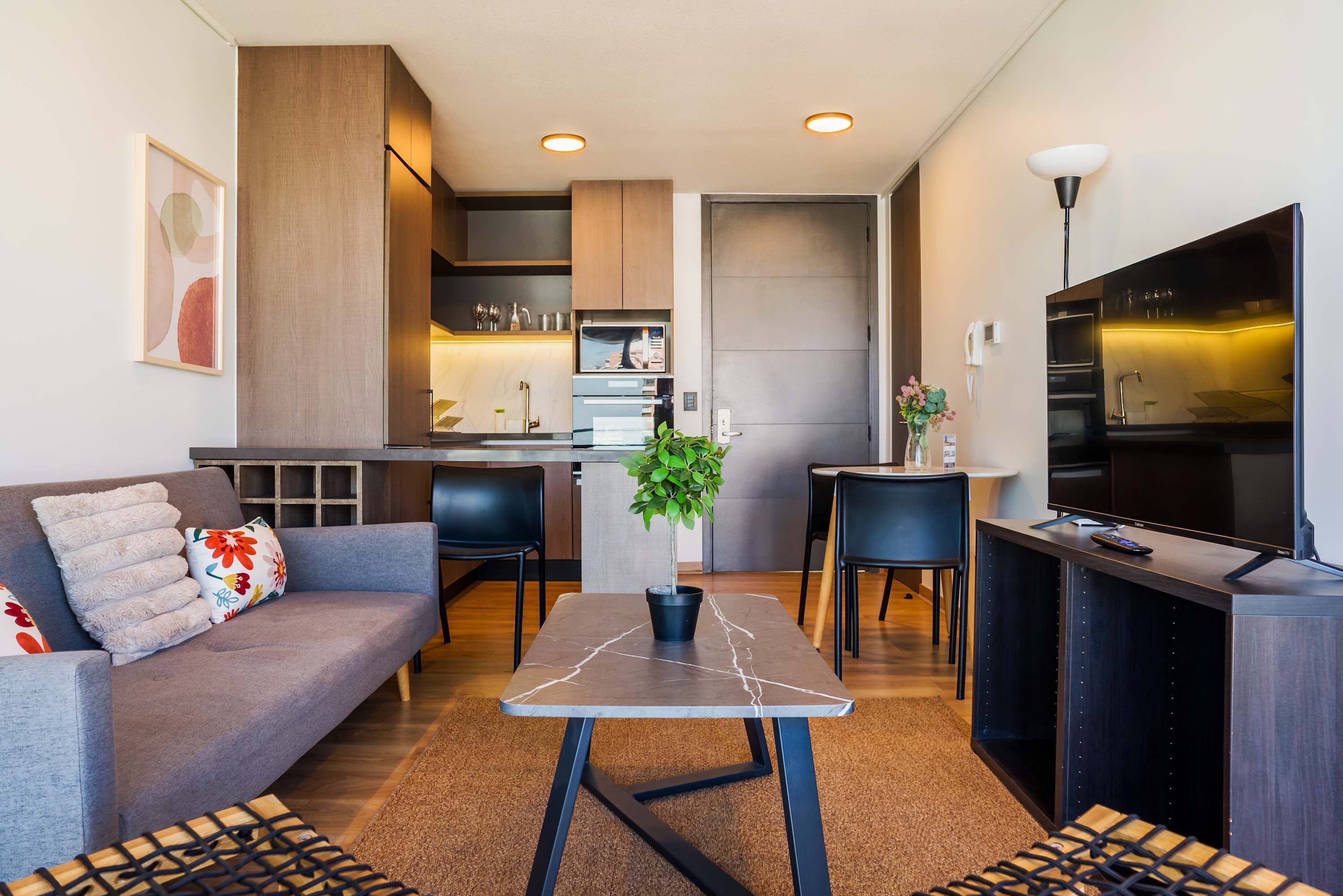 Un salon moderne avec un canapé, une table basse, un téléviseur et un coin cuisine à l’arrière-plan.