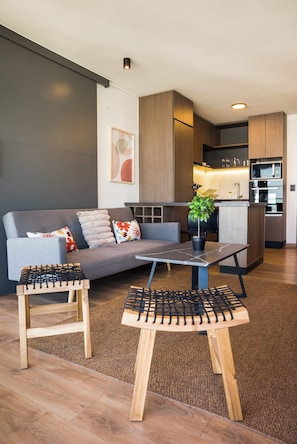 A modern living area with a sofa, coffee table, and side tables, a kitchen with appliances, and a plant. - Chic 2BR Haven in the Heart of Las Condes Oasis (Unknown)