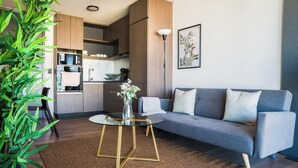 A modern living space with a grey sofa, a glass coffee table, and a kitchen area with wooden cabinets and a microwave. - Prime 2BR Oasis in the Heart of Las Condes (Unknown)