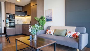 Een moderne woonkamer met een grijze bank, een bijzettafeltje, en een keuken met houten kastjes en een magnetron.
