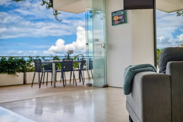 A balcony with a view of the sky and clouds, a table with chairs, and a sofa with a blanket.