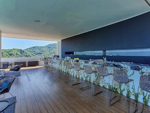 Eine großzügige Außenterrasse mit Holzboden, Korbstühlen und einer Bar mit Blick auf die Stadt und die Hügel.