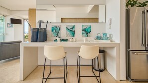 Uma cozinha moderna com dois bancos altos, uma geladeira e arte abstrata na parede.