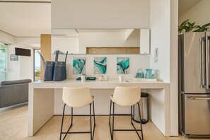 Eine moderne Küche mit zwei Barhocker, einem Kühlschrank und abstrakter Kunst an der Wand.