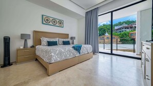Quarto moderno com cama grande, abajures, mesa de cabeceira e vista para o exterior através de uma porta de vidro deslizante.
