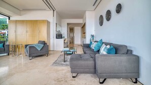 Uma sala de estar moderna com um sofá seccional cinza, uma mesa de centro e uma área de jantar com uma cozinha ao fundo.