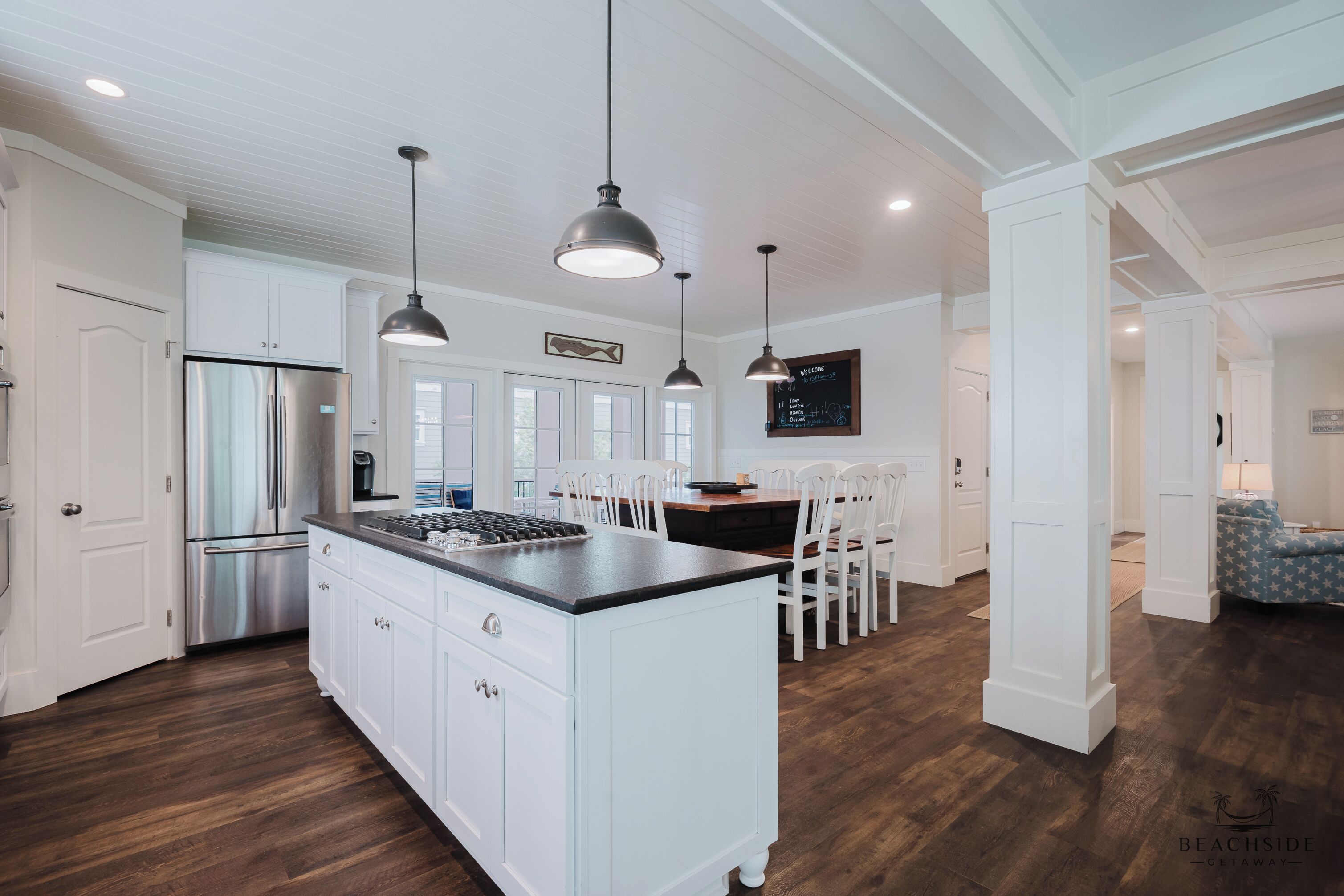 A modern kitchen with white cabinetry, a stainless steel refrigerator, and pendant lighting.