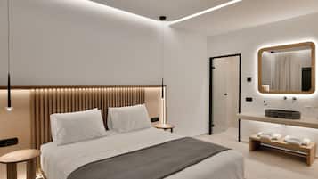 Una habitación de hotel moderna con una cama grande, mesitas de noche, un tocador con espejo y un pequeño banco con toallas.