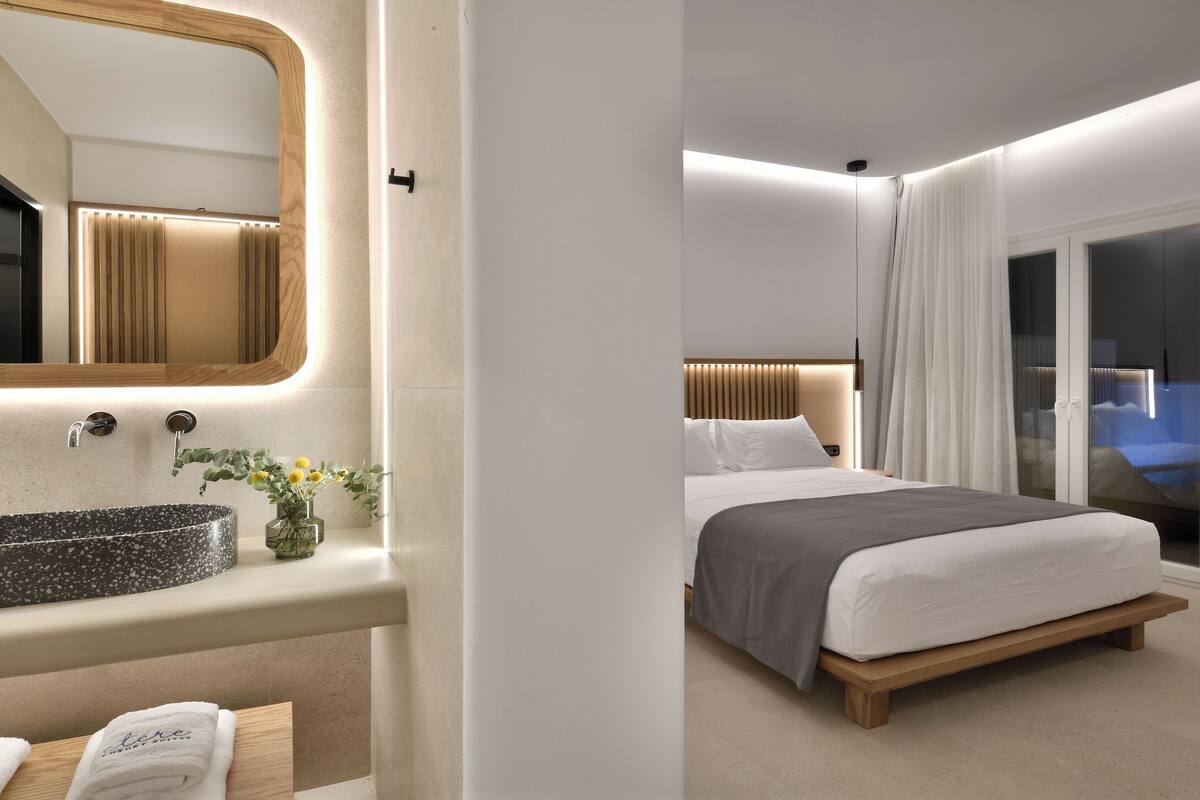 A modern hotel room with a large bed, a bathroom with a round sink, and a mirror.