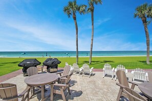 Un espace extérieur aménagé avec des tables et des chaises, offrant une vue sur une plage bordée de palmiers et sur l’océan.