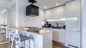 A modern kitchen with white cabinetry, a wooden countertop, and a built-in island with bar stools. - Olea Suite Pomegranate (Polignano a Mare)