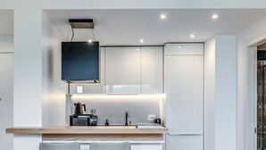 A modern kitchen with white cabinets, a wooden countertop, and a built-in TV. There are two bar stools and a round table with chairs. - Olea Suite Pomegranate (Polignano a Mare)