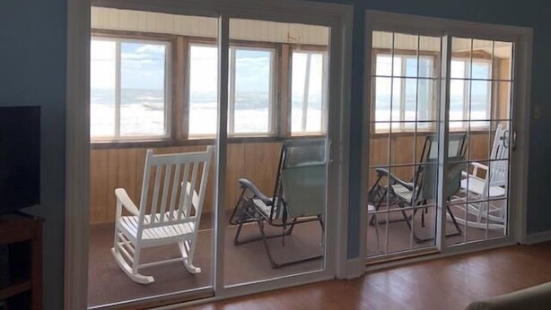 Ein Zimmer mit Blick auf den Strand, ein weißer Schaukelstuhl und ein Tisch mit Stühlen.