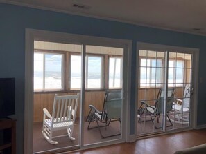 A room with a view of the beach, a white rocking chair, and a table with chairs.