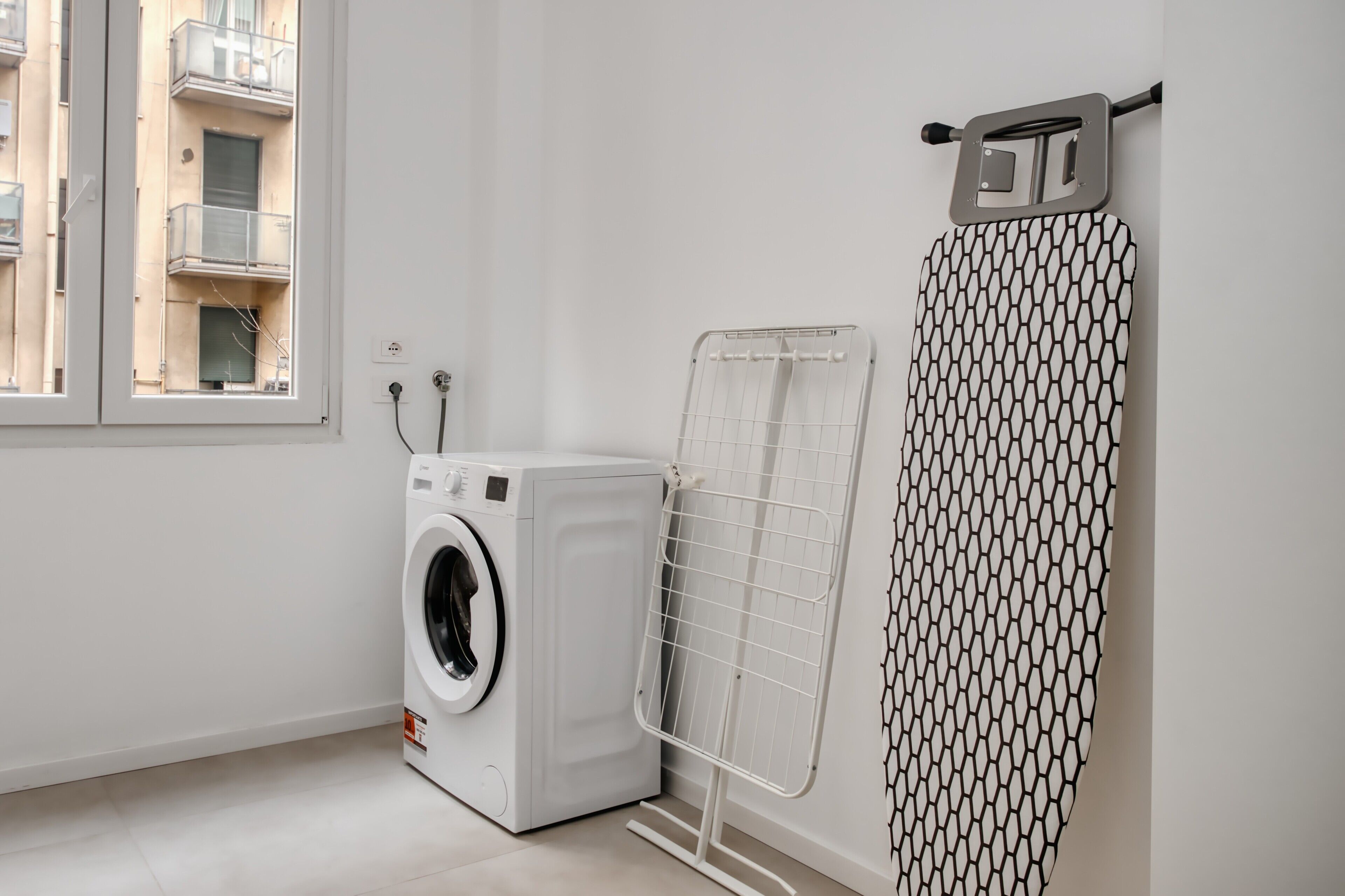 A laundry area with a washing machine, a drying rack, and a window with a view of buildings.