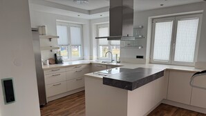 A modern kitchen with white cabinetry, a marble countertop, and wooden flooring. - 1-bedroom apartment in Vilseck with WiFi, walking distance to base & food trucks (Vilseck)